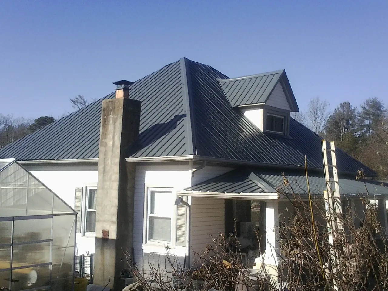 Dark blue standing seam metal roof on a white farmhouse with dormer — Slate & Tile Roof Repair by Roofing Brothers in Gayville