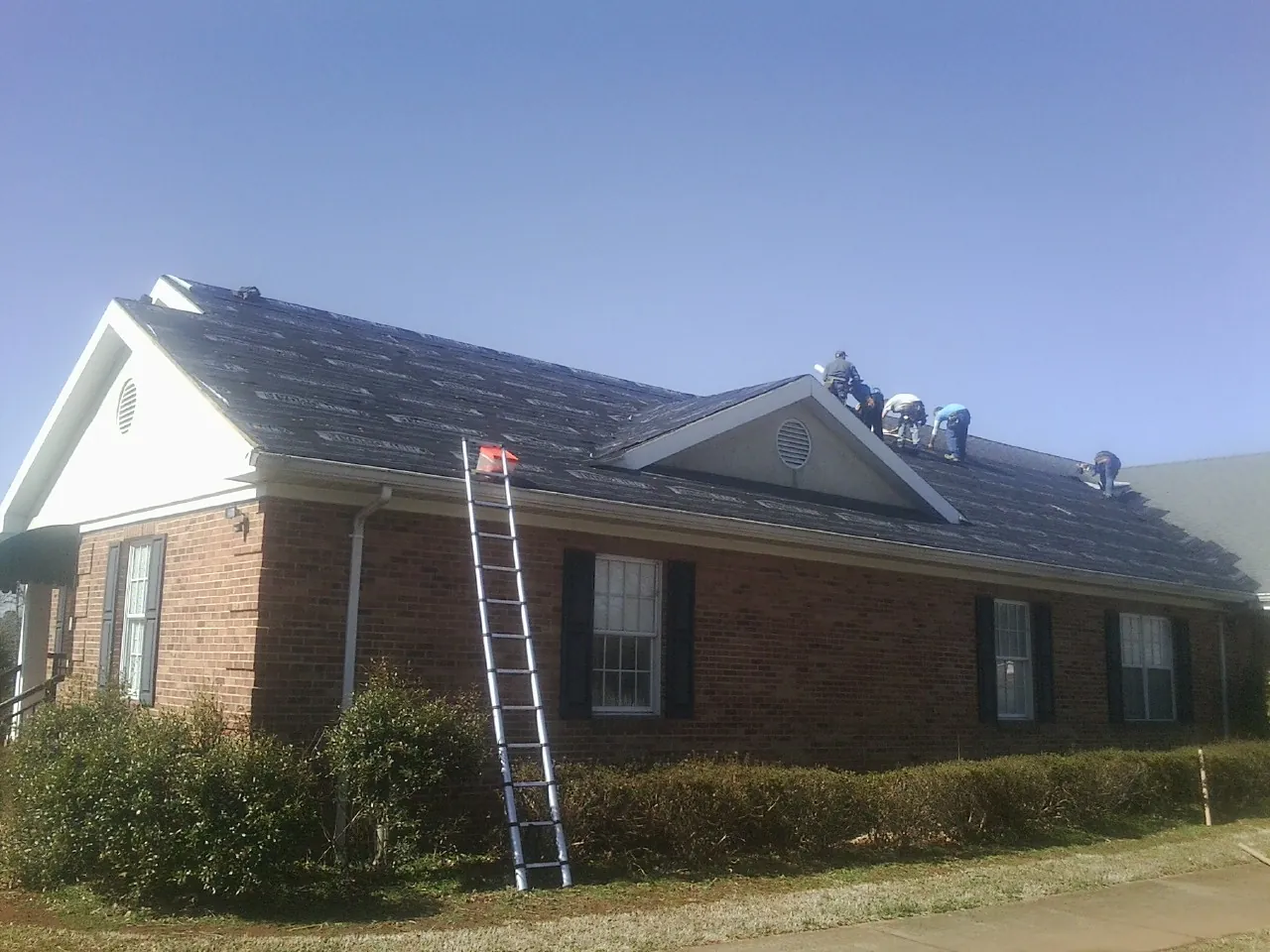 Crew tearing shingles off a brick ranch roof with a ladder set — Metal Roof Repair work by our crew in Gayville