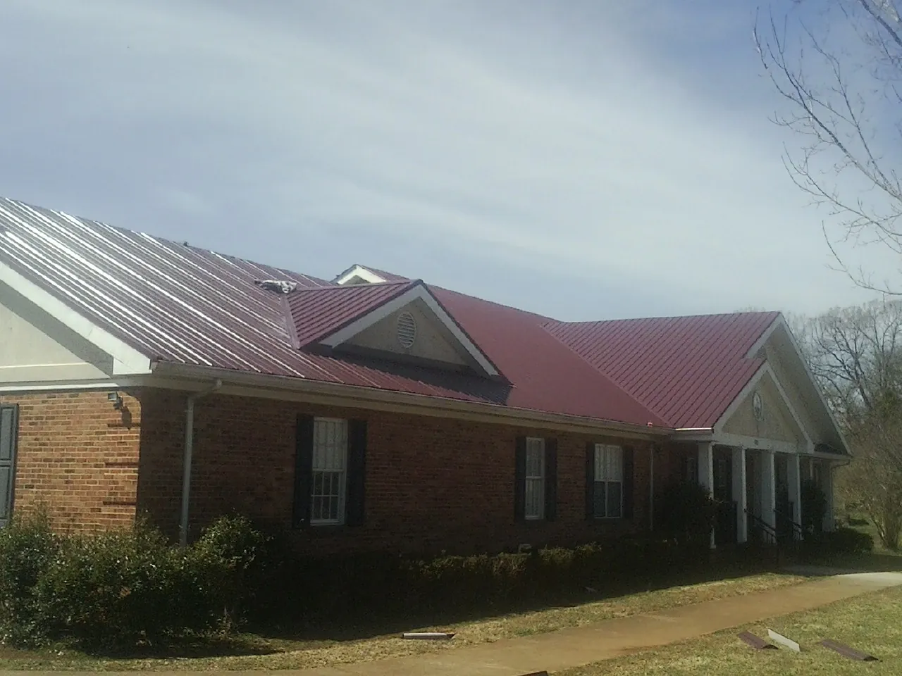 Red metal roof with gabled entries on a long brick building, from a Hail Damage Roof Repair job in Gayville