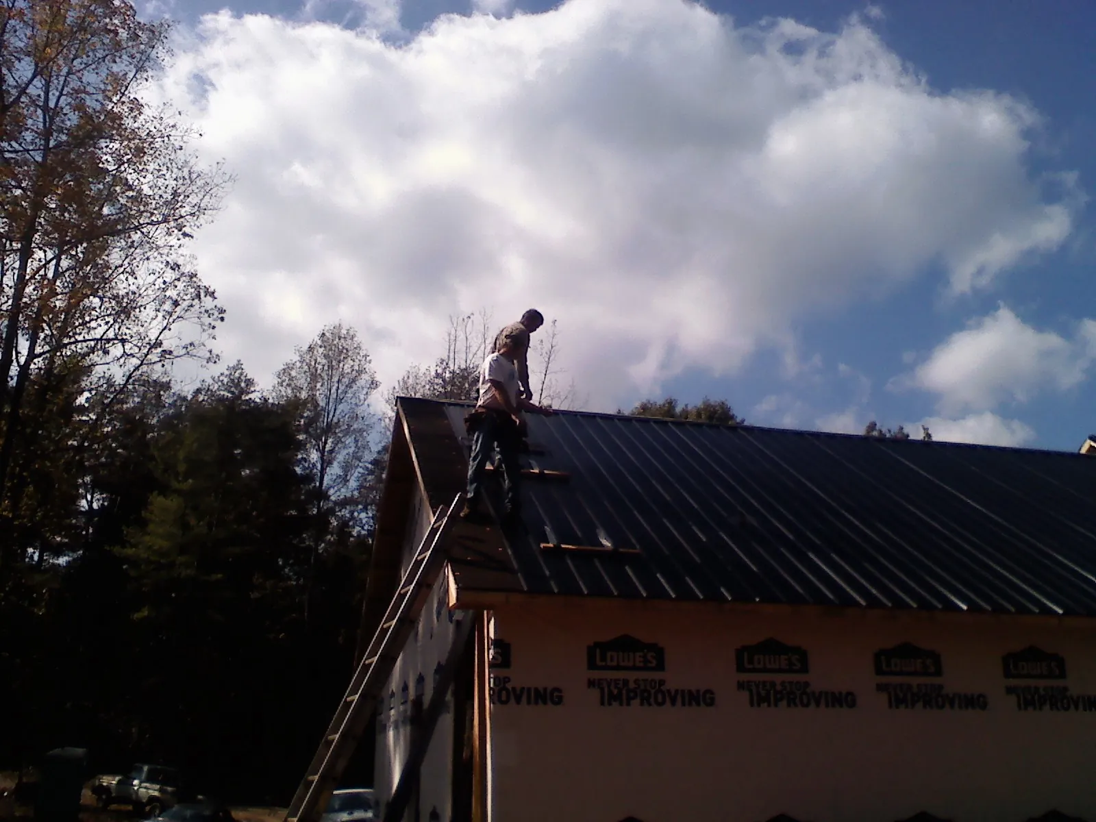 Roofer fastening dark metal panels high against a cloudy sky, from a Roof Inspection job in Gayville